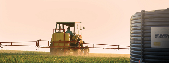 Photo of farmer spraying crops with tank in foreground